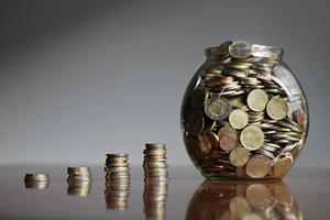 mucchi crescenti di monete che terminano in un barattolo di vetro pieno di denaro - inflazione o strategia di investimento di successo foto