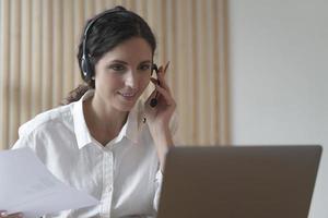 agente di call center di giovane donna italiana in cuffia che parla con il cliente, consultando il cliente online foto