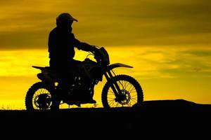 silhouette nera di motociclista con moto su sfondo giallo cielo al tramonto foto