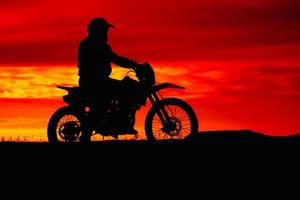 silhouette nera di motociclista con moto su sfondo rosso cielo al tramonto foto