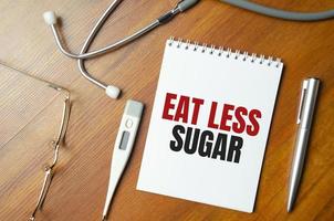 mangia meno parole di zucchero su taccuino e stetoscopio su fondo di legno foto
