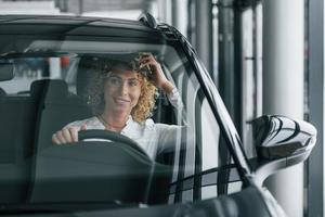 seduto al posto di guida. la donna con i capelli biondi ricci è in autosalone foto