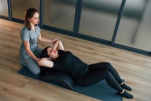 usando il tappetino da yoga. la donna è in centro sanitario e viene aiutata dal medico foto