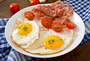 colazione all'inglese - pane tostato, uova, pancetta e verdure in stile rustico su fondo di legno foto