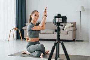 fare lezioni davanti alla telecamera. la giovane donna con un tipo di corpo snello e in abiti da yoga è a casa foto