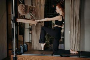 allenatore di pilates in forma snella che mostra esercizi di stretching su cadillac reformer foto