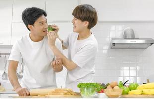 giovane coppia asiatica maschio lgbt felice e godersi il tempo trascorso insieme durante la cottura con la faccia sorridente in cucina bianca sullo sfondo della casa. foto