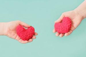 mani femminili che tengono cuori rossi lavorati a maglia su sfondo turchese. concetto di amore e san valentino. relazione e famiglia, appuntamenti e fidanzamento. foto