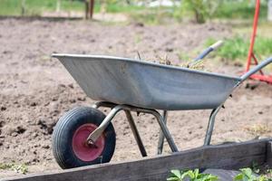 carriola da giardino riempita di terra o compost presso la fattoria. pulizia stagionale del giardino prima dell'autunno. sulla strada. carriola monociclo da giardino in metallo piena di erbacce e rami. foto