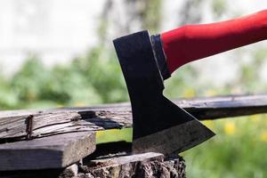 una nuova ascia moderna con un manico rosso sporge da un ceppo di legno contro un prato verde in una giornata di sole estivo. l'ascia conficcata nel ceppo. lama dell'ascia in un ceppo. foto