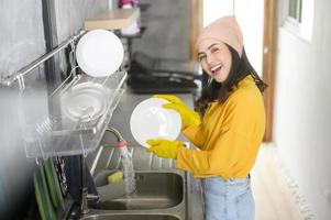 giovane donna felice che indossa guanti gialli che lava i piatti in cucina a casa foto