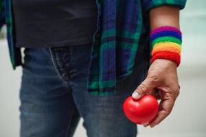 donna asiatica che tiene un hert rosso con bandiera arcobaleno, diritti dei simboli lgbt e uguaglianza di genere, mese dell'orgoglio lgbt a giugno. foto