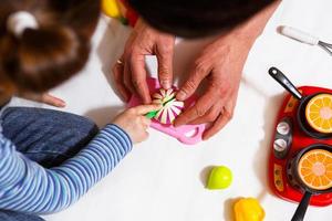 papà e figlia giocano con frutta e verdura di plastica a fette con il velcro, cuociono il cibo su un fornello giocattolo in una ciotola. cucina per bambini, una ragazza impara a cucinare. sfondo bianco, primo piano. festa del papà foto