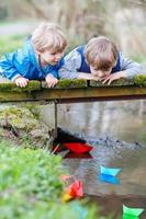 due fratellini che giocano con le barche di carta su un fiume foto