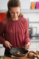 giovane casalinga felice che cucina i funghi foto