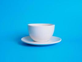 fotografia di vista superiore della tazza di caffè bianca su un piattino bianco l'interno della ceramica di vetro sembra vuoto. aspettando che il caffè caldo venga riempito da bere per sentirsi riposati e vigili su uno sfondo blu. foto