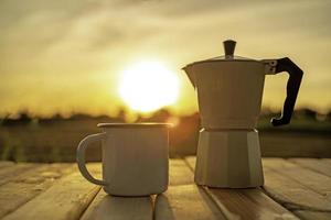 caffè caldo e moka con lo sfondo dell'alba. tazza di caffè sul tavolo di legno con lo sfondo dell'alba. fuoco morbido. foto