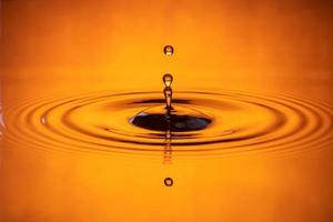 goccia d'acqua spruzzata in un bicchiere d'acqua di colore arancione che gocciola e riflette l'acqua. foto