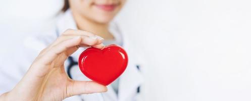 giovane dottoressa con lo stetoscopio che tiene il cuore rosso, concetto di assistenza sanitaria cardiologo foto