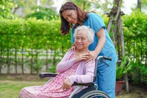 il caregiver aiuta e supporta il paziente asiatico anziano o anziano della donna sulla sedia a rotelle nel parco, concetto medico sano e forte. foto
