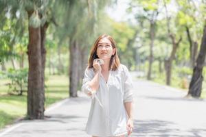 donna che cammina nel parco con un colpo di sole in estate calda, giovane bella ragazza che asciuga il sudore usando un panno in una calda giornata estiva in un parco foto