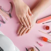 procedura di cura delle unghie in un salone di bellezza. mani femminili e strumenti per manicure su sfondo rosa. concetto di cura del corpo spa. foto