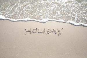 la parola vacanza scritta nella sabbia in lettere maiuscole. foto