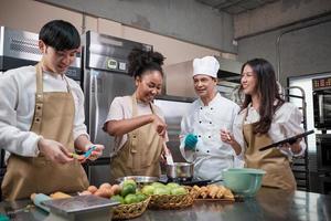 corso di cucina per hobby, lo chef maschio senior in uniforme da cuoco insegna ai giovani studenti delle lezioni di cucina a preparare, mescolare e mescolare gli ingredienti per i pasticcini, le torte di frutta nella cucina in acciaio inossidabile del ristorante. foto