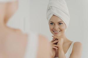 giovane donna in buona salute con la pelle pulita che sorride mentre applica la crema facciale foto