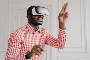 impressionato ragazzo di etnia africana in occhiali vr headset godendo la realtà virtuale online al lavoro foto
