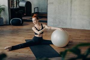 giovane donna in posizione divisa che si esercita con fitball in palestra foto