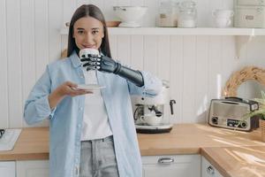 la donna europea disabile felice sta tenendo una tazza di caffè con la mano informatica. routine della persona amputata. foto