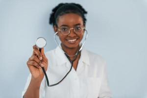 medico con lo stetoscopio. la giovane donna afroamericana è su sfondo bianco foto