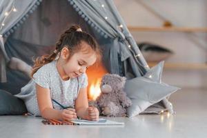 con libro. bambina carina che gioca nella tenda che si trova nella stanza domestica foto