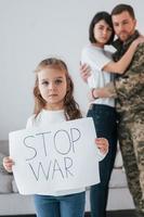 ragazza con banner con testo stop war su di esso. il soldato in uniforme è a casa con la moglie e la figlia foto