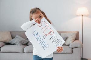 bambina in piedi a casa e con in mano un banner con stop war nel testo dell'ucraina foto