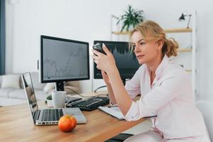 leggere le informazioni dallo smartphone. agente di borsa femminile in abbigliamento formale sta lavorando in ufficio foto