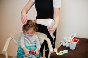 mamma con la figlia del bambino che fanno insieme la routine quotidiana. la madre sta spazzolando e asciugando i capelli del bambino dopo la doccia. foto