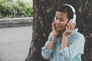 la donna si rilassa nel parco. Si siede sotto un grande albero e si sente bene. lei fa un respiro profondo sull'aria fresca. concetto di foto relax tempo e buona salute.