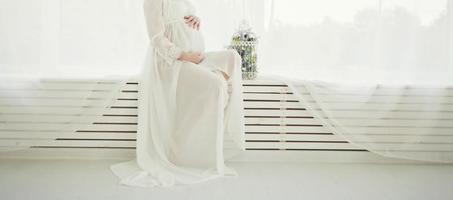 donna incinta in abito seduto vicino alla finestra foto