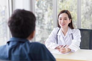 una dottoressa professionista asiatica che indossa un camice medico parla con un paziente uomo per consultarlo e suggerirgli informazioni sanitarie nella sala d'esame dell'ospedale. foto