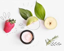 maschera per la cura del viso di mela e fragola su sfondo bianco. ingredienti cosmetici biologici naturali. crema in vasetto di vetro. vista dall'alto foto