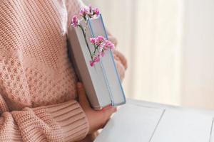 una ragazza con libri e fiori rosa, vista ritagliata. concetto di primavera in arrivo. contenuti blogger, lettura e ritorno a scuola foto