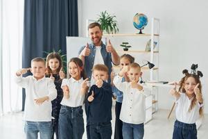 mostrando i pollici in su. gruppo di bambini studenti in classe a scuola con l'insegnante foto