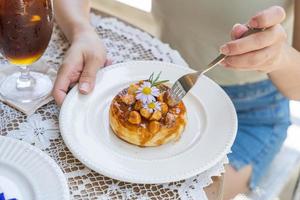 la forcella usata a mano della donna mangia le ciambelle o i cronuts fritti fatti in casa di pasta sfoglia. topping croissant e ciambella con noci macadamia e salsa al caramello. foto