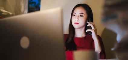 donna freelance che usa il telefono durante gli straordinari che lavorano presso l'ufficio a casa foto