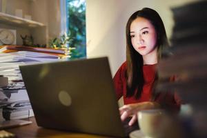 donna di affari asiatica che lavora al computer portatile nell'ufficio di casa. lavoro straordinario facendo progetto di scadenza