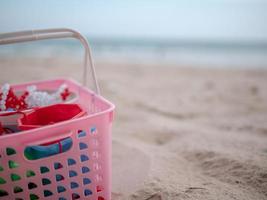 giocattoli per bambini in un cestino di plastica rosa messo sulla spiaggia di sabbia foto