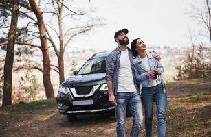 persone positive. abbracciare e godersi la natura. la coppia è arrivata nella foresta con la loro auto nera nuova di zecca foto