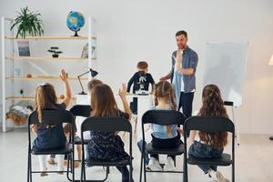 guardando il ragazzo con il microscopio che è sul tavolo. gruppo di bambini studenti in classe a scuola con l'insegnante foto